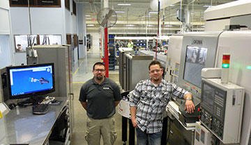 CNC programmers, Matt Smith and Rich Stenberg pose between their shop-floor GibbsCAM workstation and the Okuma MacTurn 250 to demonstrate proximity. “We just need to tie the MacTurn into the network to send programs directly, because now it requires a thumb drive and a three-foot walk,” says Smith.