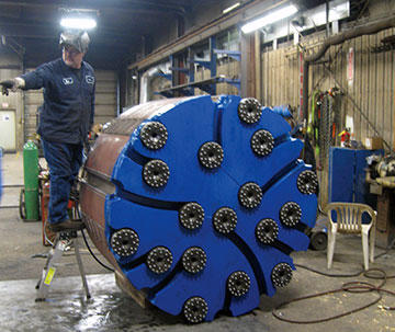 A drill sometimes includes many bits for cutting the rock, as is the case with this one about to be welded in the company’s fabrication area