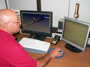Brent Schmidt reviews a SolidWorks print of nickel 200 tube for Rosemount Aerospace, while the monitor on the left displays GibbsCAM MTM’s Cut Part Rendering verifying tool path for the Citizen C32 as it machines the end of the same part.