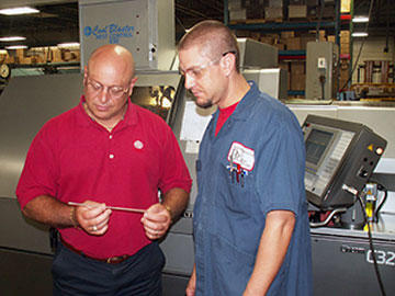 Manufacturing engineer and GibbsCAM programmer Brent Schmidt, left, discusses long, narrow Rockwell Collins part with Citizen-Cincom C32 machinist Joel Boulton, who was hired specifically for his expertise with the Swiss turn machine.