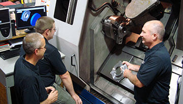 Chuck Paul (right) discusses a part, one of a pair of bearing-housing covers the shop produces for a railroad repair machine company with Danny Burchfield (left) and Greg Hauth.