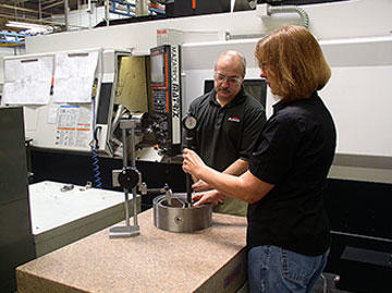 Tamara Hawn and Tool and Development supervisor Paul Nanney inspect a component made on the Mazak Integrex (behind them), for a “large bore diesel liner,” a fixture for a Sunnen customer honing system.