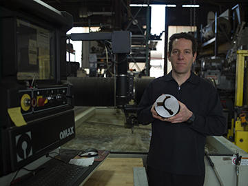 Binkert holds a 3" thick chrome-moly slug from which he cut a prototype part with GibbsCAM and the Omax Waterjet for the city of San Francisco.