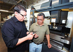 Esdras Giron (left) reviews impeller with machine operator Jonathan Duarte in front of Haas VF-4 with trunnion machining an impeller.