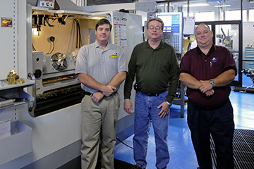 Nash Community College began its machining technology program in 1987. Instructors Brian Worley, Craig Bidwell and George Shook (left to right) with the trunnion-equipped machine tool that machined the brass nozzle after the NC program was tested with simulation.