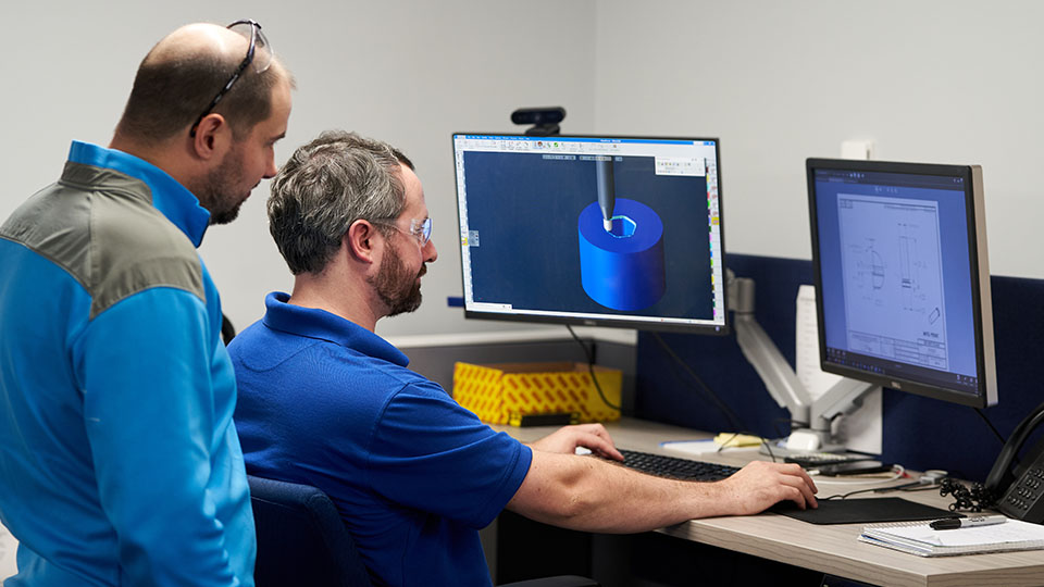 Senior Manager Jason Esch watches as Project Programmer Mark Scanlon reviews a GibbsCAM program.